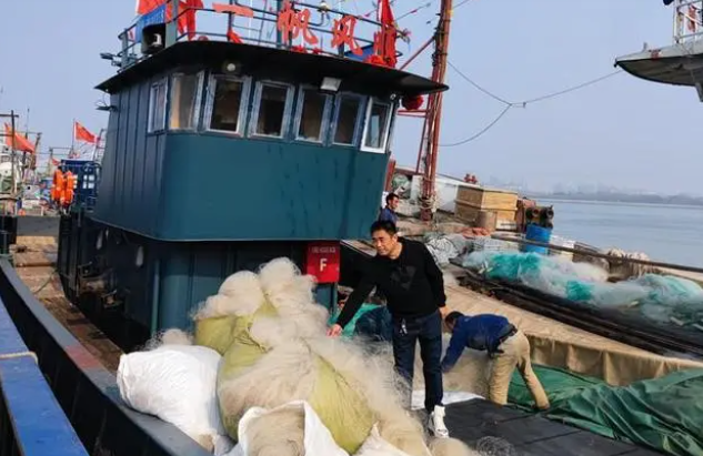 北塘漁港漁戶吳立民站在一艘剛剛回港的漁船上，向岸上的人們介紹自己的新船。